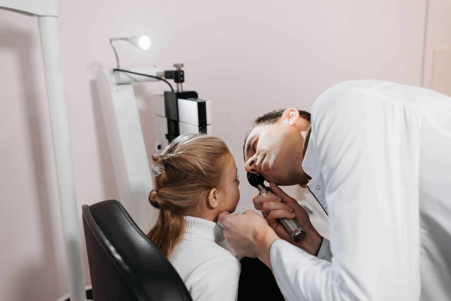 A doctor looking into a young girl's ear with an otoscope