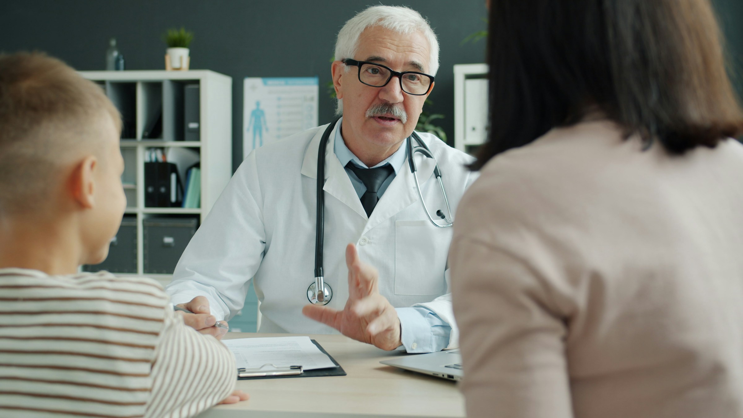 A doctor talking with a child and parent across his desk